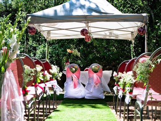 Mariage en plein air entouré d'hébergements insolites, chaises rouges décorées, nature luxuriante. Auberge de la Tuilière