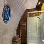 Salle de bain chaleureuse façon cabane perchée : parquet à motifs, éléments naturels et fenêtre ronde. Auberge de la Tuilière