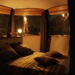 Cabane perchée douillette, fenêtres courbes sur forêt nocturne, ambiance chaleureuse et insolite. Auberge de la Tuilière