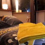 Chambre douillette, lumière tamisée, ambiance insolite, lit graphique noir-blanc-jaune, rideaux nature. Auberge de la Tuilière