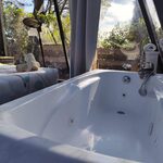 Baignoire à jets dans une cabane vitrée, lit coloré, verdure luxuriante, ambiance insolite et cosy. Auberge de la Tuilière