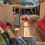Seau de champagne sur table en bois, ambiance chaleureuse dans bus aménagé aux murs boisés, banquettes rouges. Auberge de la Tuilière