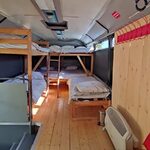 Intérieur chaleureux de bus réaménagé, bois, lits superposés ; hébergement insolite baigné de lumière. Auberge de la Tuilière