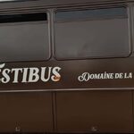 Bus marron "FESTIBUS", "Domaine de la Tuilière", hébergements insolites, fenêtre sombre, roue visible. Auberge de la Tuilière