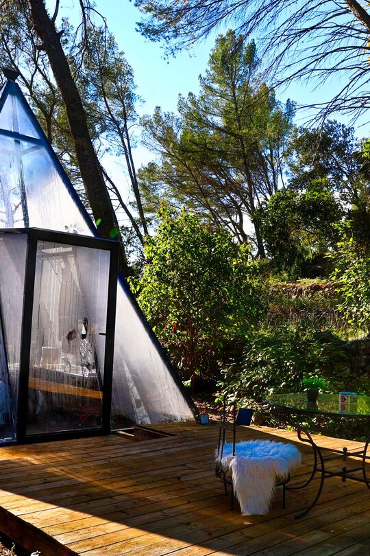 Tipyramide transparente sur terrasse bois, chaises cosy dans la verdure, parenthèse insolite et sereine. Auberge de la Tuilière