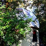Tipyramide blanche nichée sous les arbres, charme insolite, ombre et jeux de lumière au sol. Auberge de la Tuilière