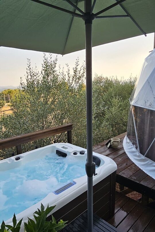 Bain à remous sur terrasse bois, dôme blanc insolite, arbres et guirlandes lumineuses, nature paisible. Auberge de la Tuilière