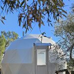 Dôme géodésique blanc sur terrasse bois, "Bienvenue", entouré d'arbres, expérience insolite en pleine nature. Auberge de la Tuilière