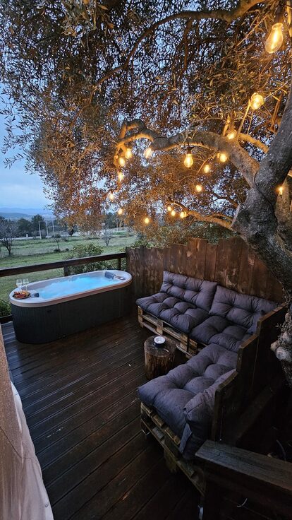 Terrasse en bois avec bain bouillonnant, assises palettes, guirlande suspendue près d'hébergements insolites. Auberge de la Tuilière