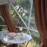 Table blanche et chaises design face à de larges fenêtres, parfaite pour une escapade insolite en nature. Auberge de la Tuilière