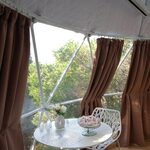 Table ronde, chaises design et douce lumière, au cœur d'une cabane perchée entourée d'arbres. Auberge de la Tuilière