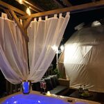 Bain chauffant sous pergola, rideaux blancs et campalune lumineux pour un séjour insolite et intimiste. Auberge de la Tuilière